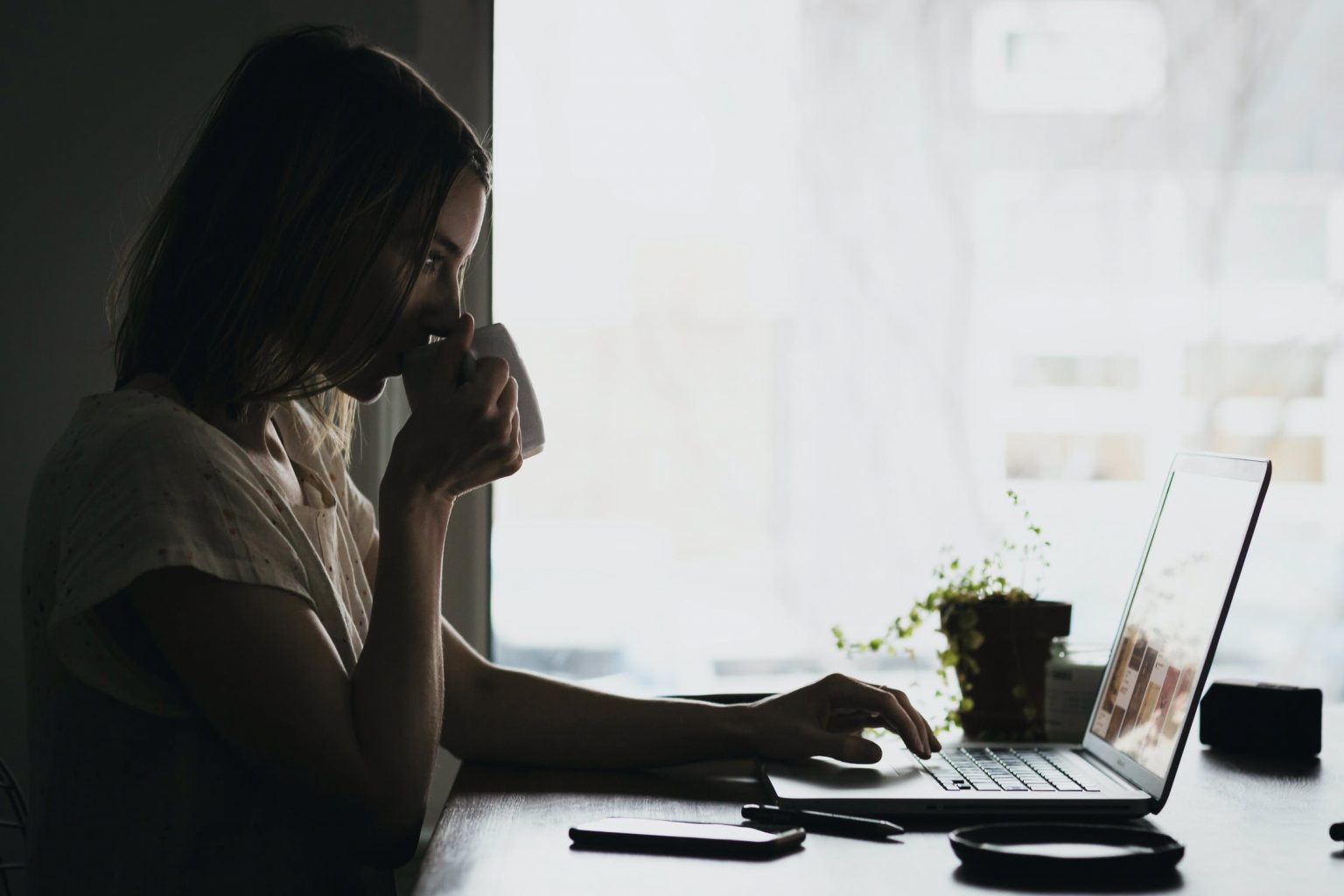 A woman drinking coffee while looking for a personal injury lawyer on her laptop.