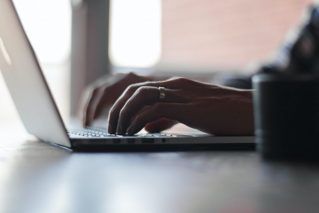 Person with a ring, typing on a laptop, negotiating with an auto insurance company after an accident.