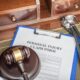 A "Personal Injury Claim Form" on a clipboard, next to a gavel and a stethoscope, on a wooden desk.