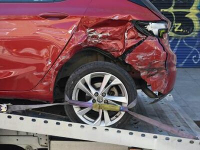 Red car with severe side collision damage loaded on a tow truck flatbed