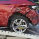 Red car with severe side collision damage loaded on a tow truck flatbed