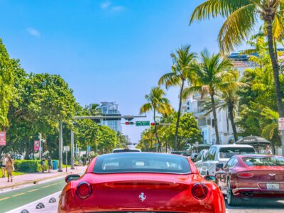 red car driving down the road near palm trees