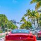 red car driving down the road near palm trees