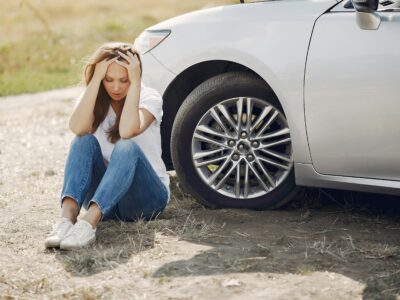 Woman sitting beside a car after an accident.